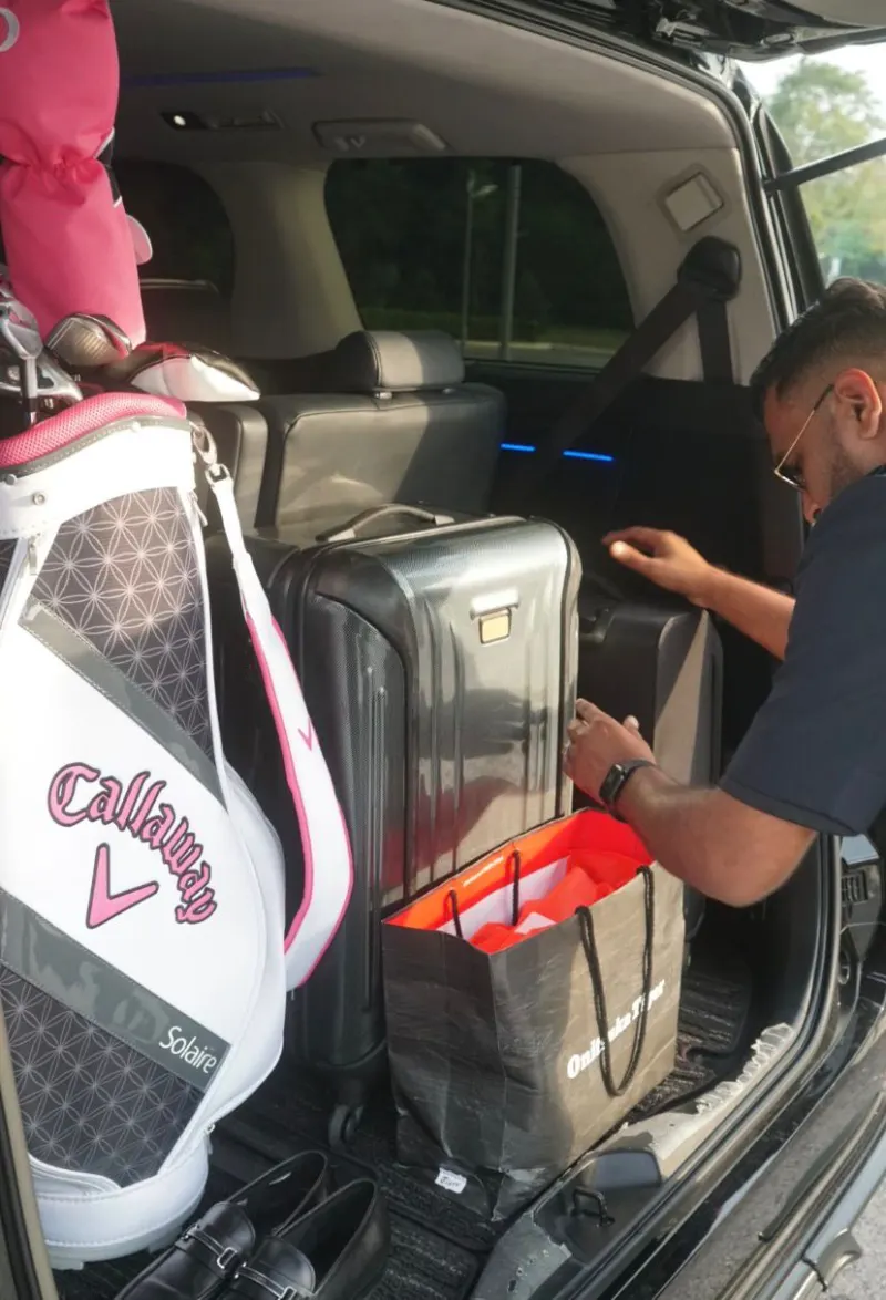Driver loading Callaway golf bag and suitcases into Alphard boot