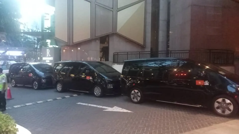 Three black MPVs with diplomatic flags at luxury hotel at night